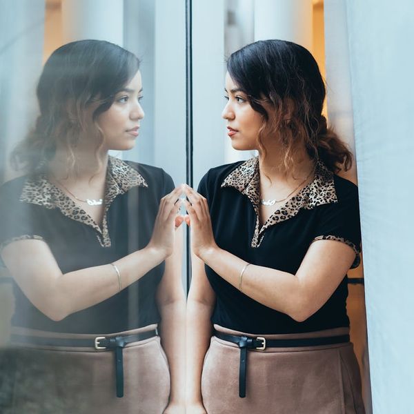 Woman looking thoughtfully through a clean window into a green landscape.